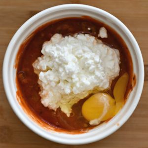 A bowl filled with marinara sauce, cottage cheese and an egg.