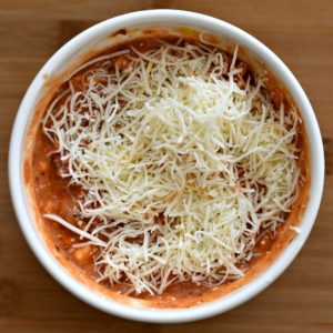 A bowl with marinara sauce and cheese on top.