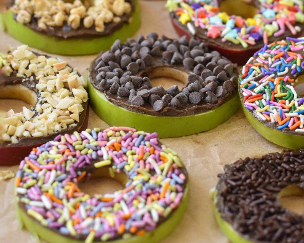 Slices of apples made to look like donuts, topped with nutella and sprinkles