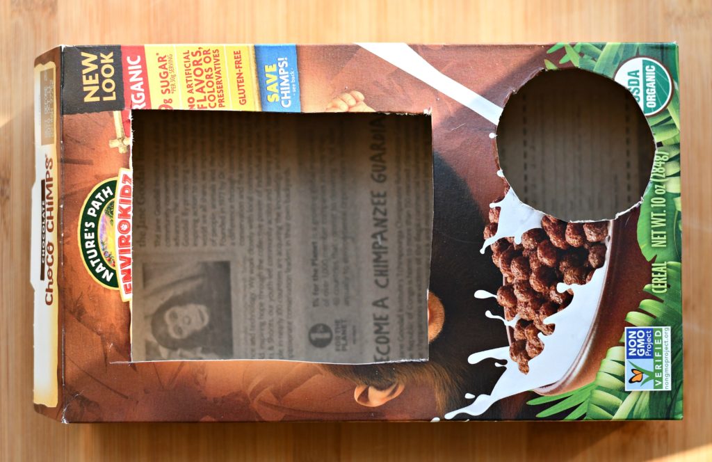 An empty cereal box with a rectangle and circle cut out of it.