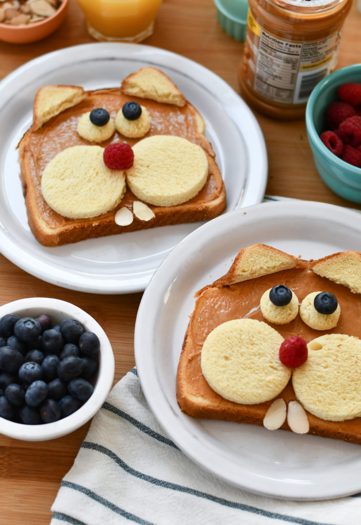 Two plates with toast made to look like groundhogs on a table with fruit in a bowl.