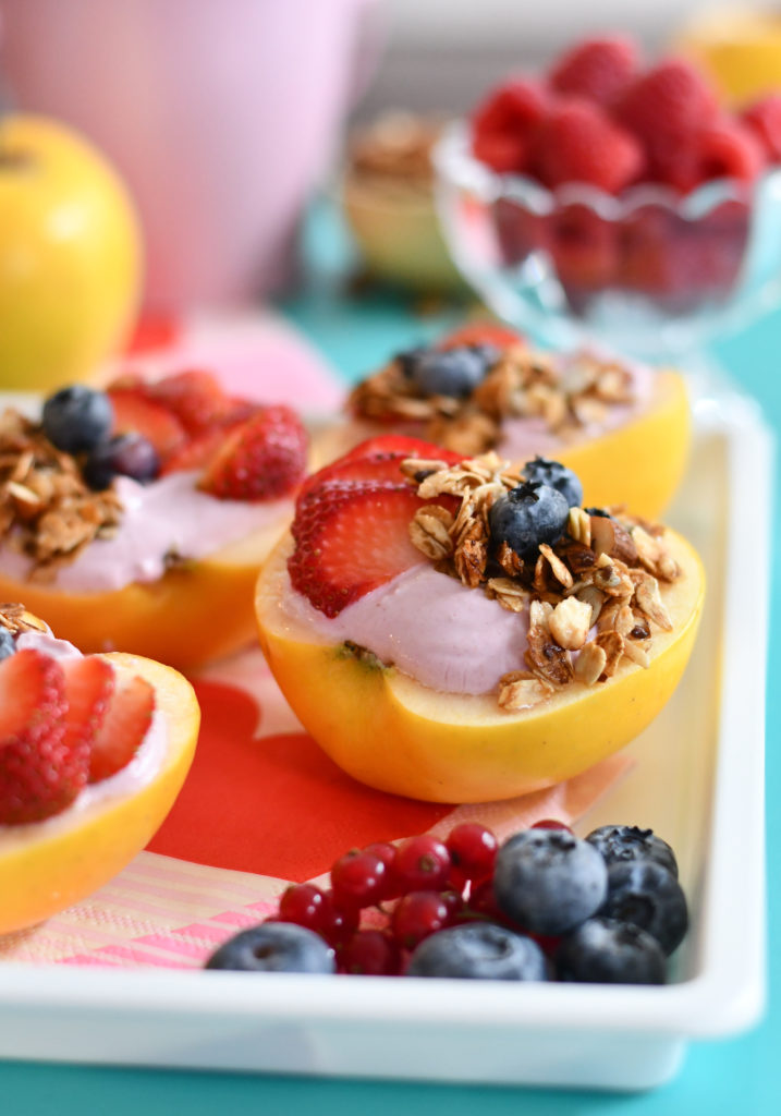 A white background with yogurt apple bowls topped with fresh fruit and granola