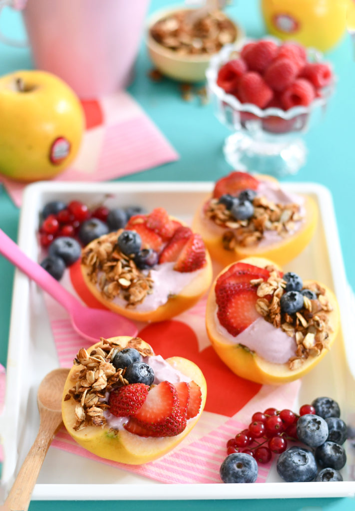 A teal background with yogurt apple bowls topped with fresh fruit and granola