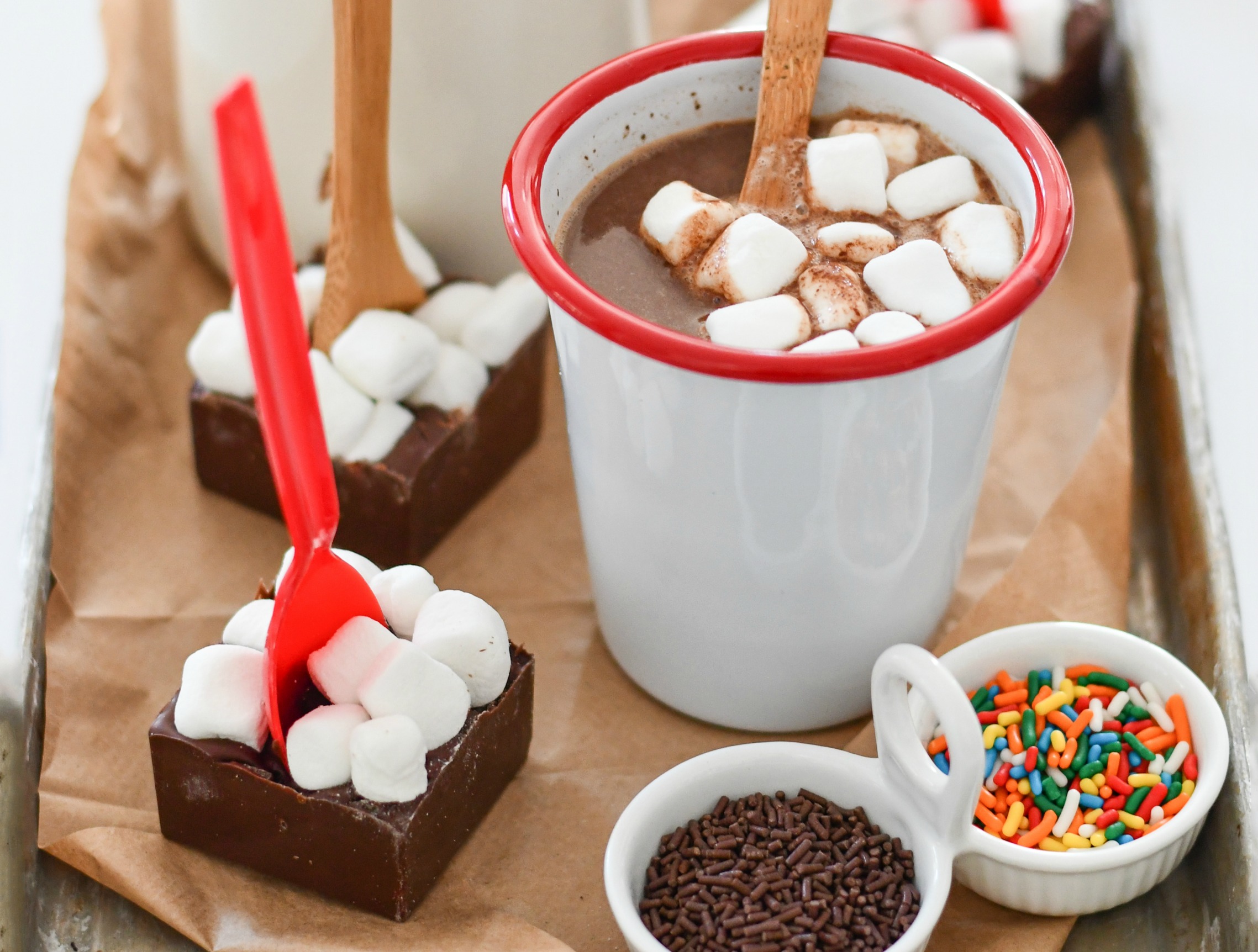 A cup of hot chocolate with marshmallows, surrounded by homemade hot chocolate spoons and sprinkles.