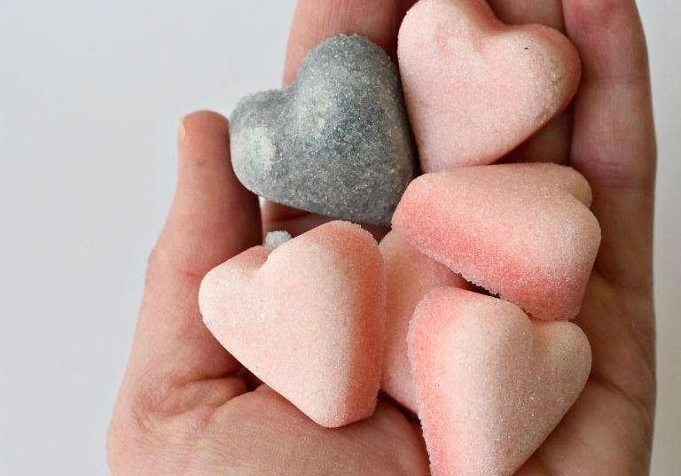 A hand holding heart-shaped sugar cubes colored pink and purple