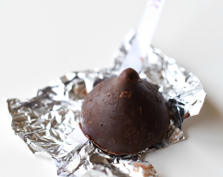A homemade nondairy chocolate Kiss with foil surrounding it on a white background