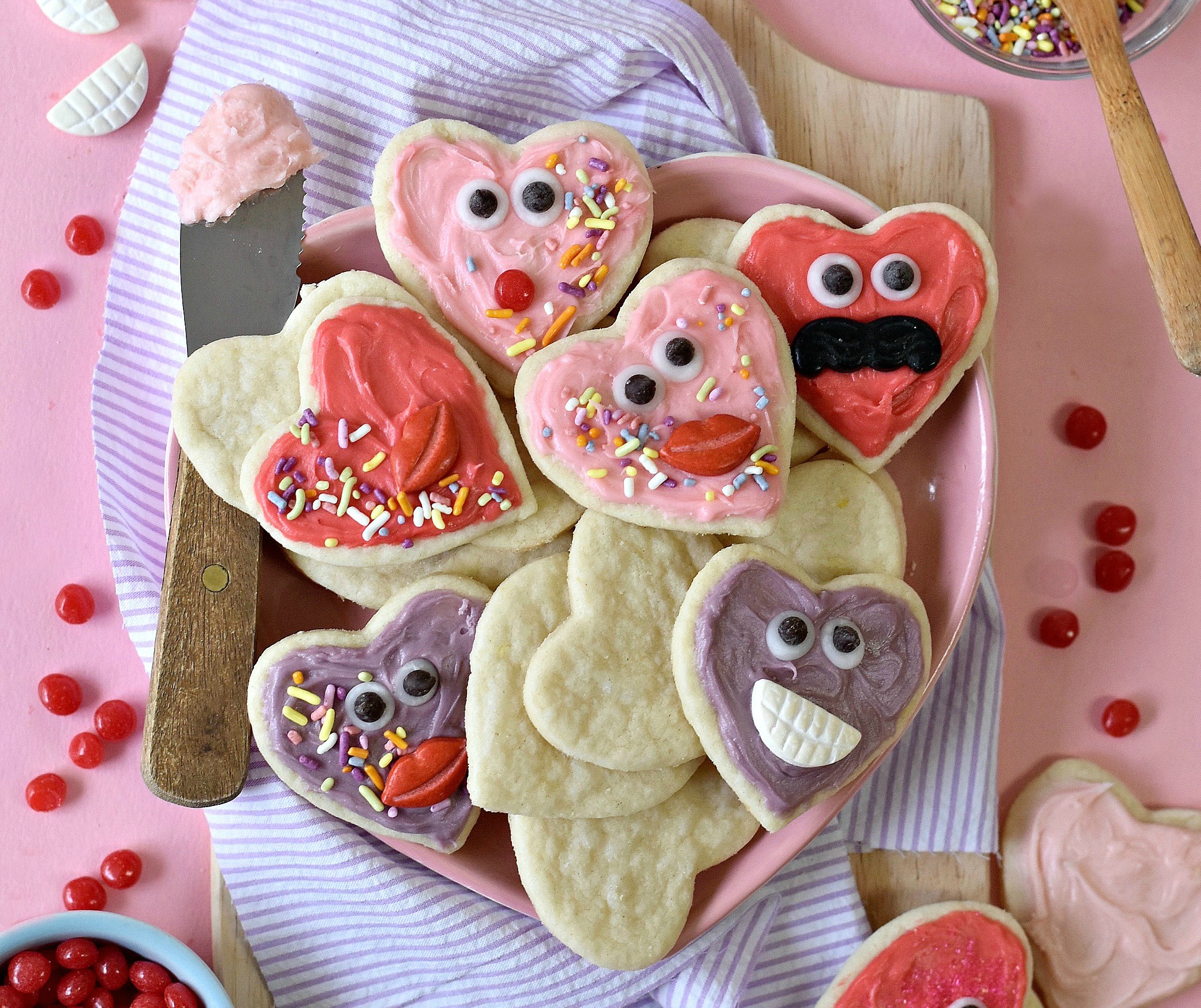 A plate full of heart shaped cookies with faces on a pink background.