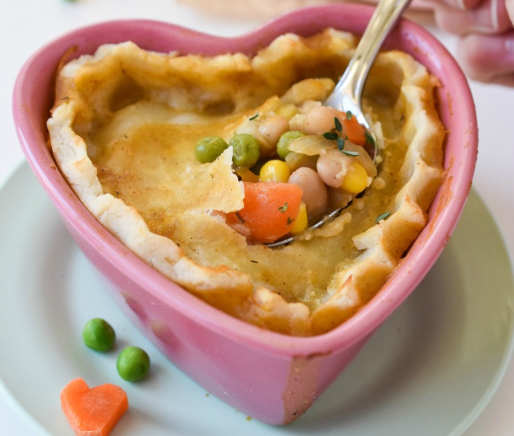 A heart shaped pot pie with a spoon digging into it, exposing veggies