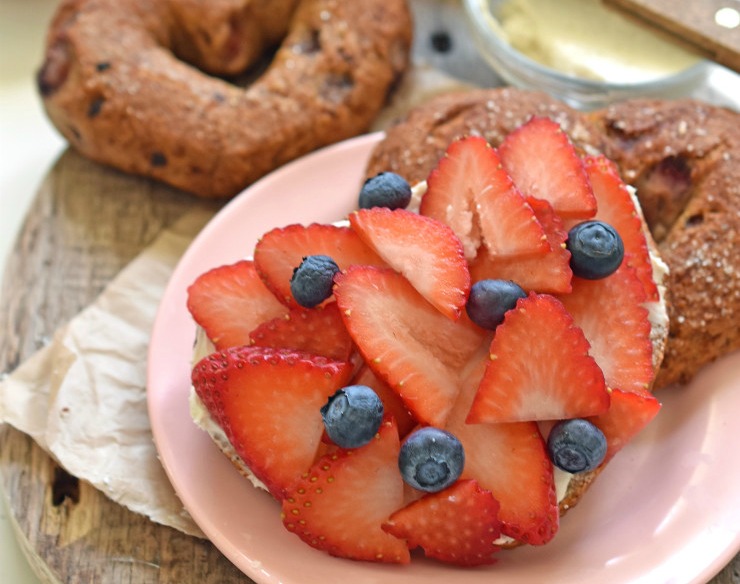 A heart-shaped bagel topped with blueberries and sliced strawberries.