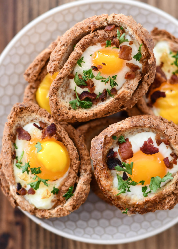 A bowl full of Egg and Toast Cups, topped with crumbled bacon and a chopped parsley.