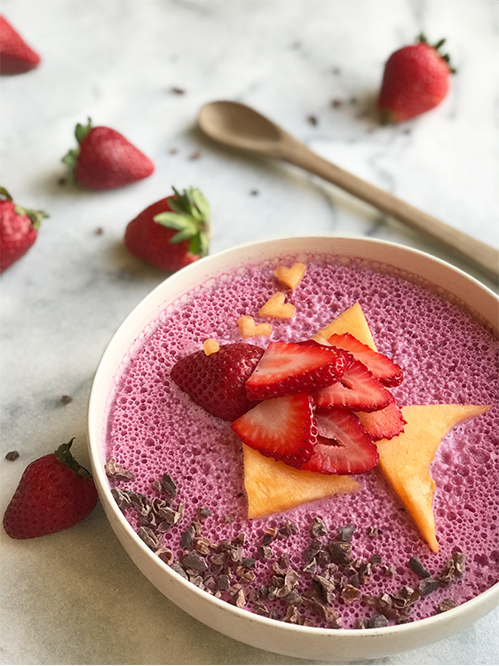 A marble background with a blueberry smoothie bowl and a strawberry fish on top.