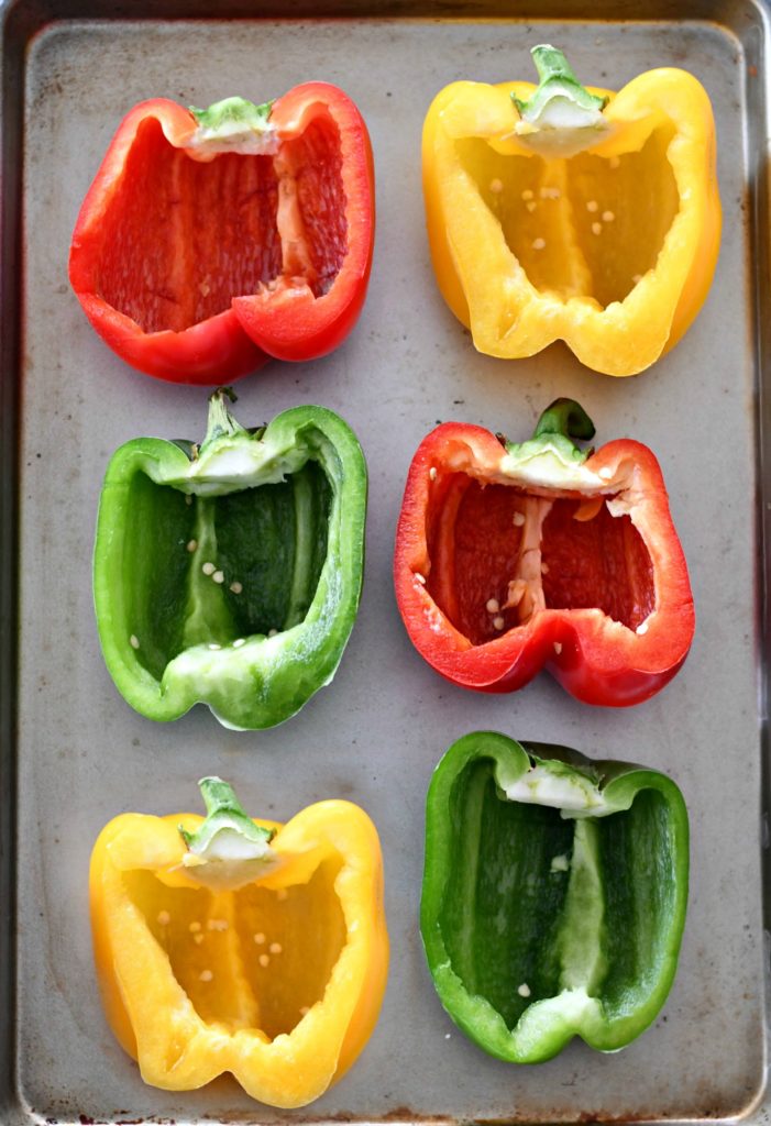 A baking sheet of red, yellow, and green bell peppers cut in half, ready to be filled for these Mexican Stuffed Peppers.