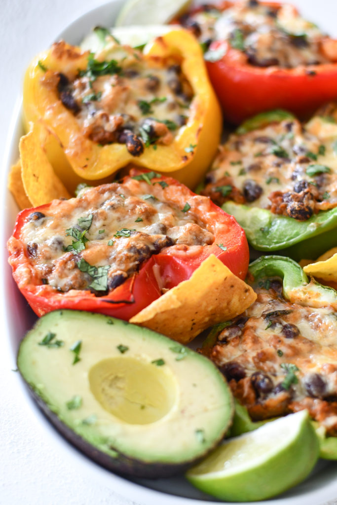 A white background with a plate of Mexican Stuffed Peppers with chips and sliced avocados. 