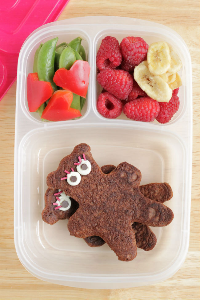 A clear lunchbox container with Teddy Bear Pancakes, heart shaped veggies, and fresh fruit.