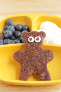 A yellow tray with chocolate Teddy Bear-shaped yogurt Pancakes, blueberries and yogurt.