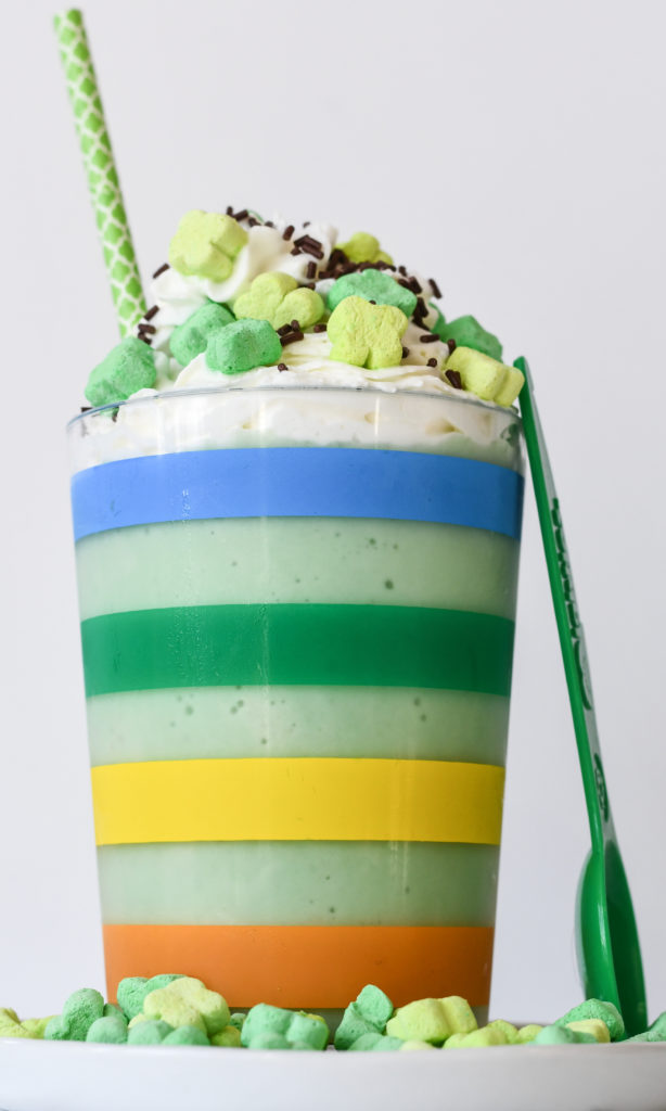A rainbow striped cup filled with a healthy green Shamrock Shake with whipped cream and sprinkles.