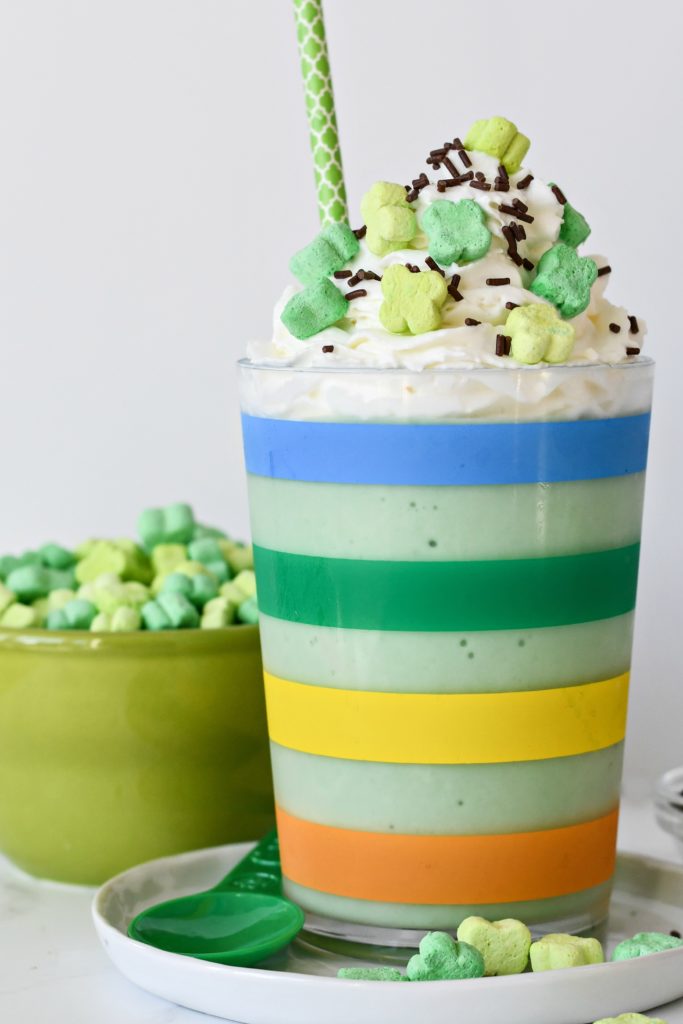 A rainbow striped cup filled with a healthy green Shamrock Shake with whipped cream and sprinkles.