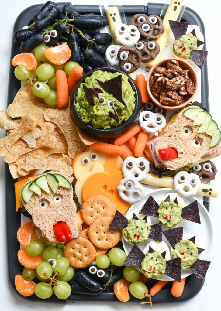 A black platter filled with fun, easy Halloween snack ideas like monster sandwiches and deviled bat eggs.