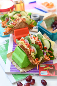 4 hummus and veggie sandwich tacos being held by taco holders with a lunchbox theme