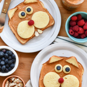 Two plates with toast made to look like groundhogs on a table with fruit in a bowl.