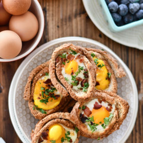 A breakfast table set with a plate of Egg and Toast Cups, surrounded by OJ, blueberries and a bowl of eggs.