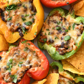 A white background with a plate of Mexican stuffed peppers with chips and sliced avocados.