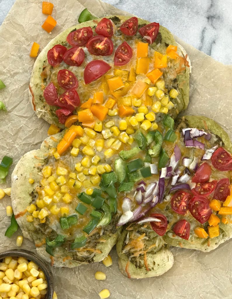 A marble slab with a shamrock pizza, topped with rainbow colored veggies