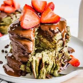 A stack of green matcha pancakes on a white place with strawberries on top