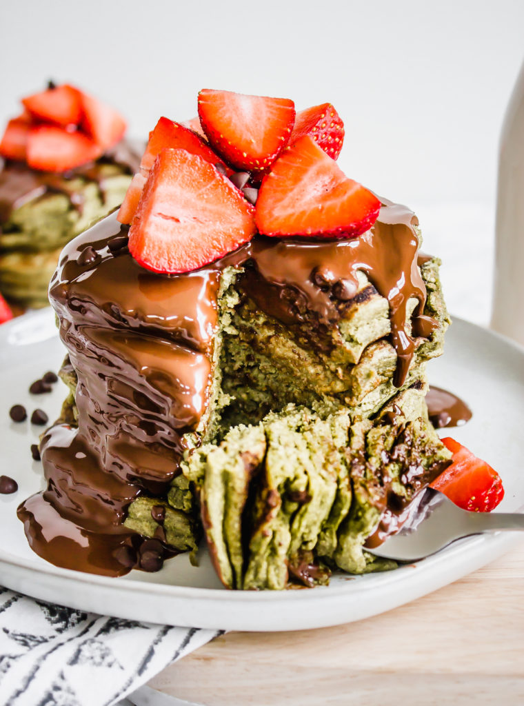 A stack of green matcha pancakes on a white place with strawberries on top