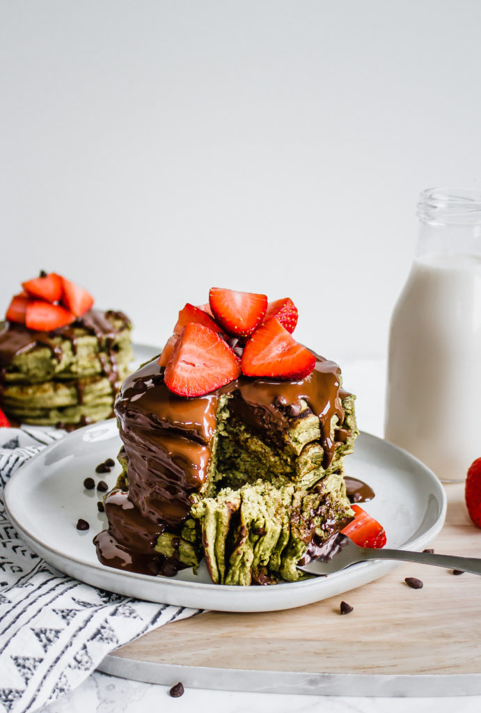A stack of green matcha pancakes on a white place with strawberries on top