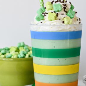 A rainbow striped cup filled with a healthy green Shamrock Shake with whipped cream and sprinkles.