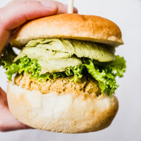 A hand holding a falafel burger on a white background