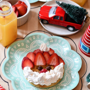 A table set with 2 plates and Christmas Breakfast Waffles made from frozen waffles, strawberries, and a whipped cream beard.